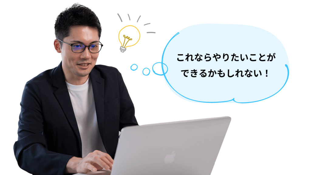 開いたパソコンを見ながら、何かを閃いた様子で微笑むスーツ姿の男性