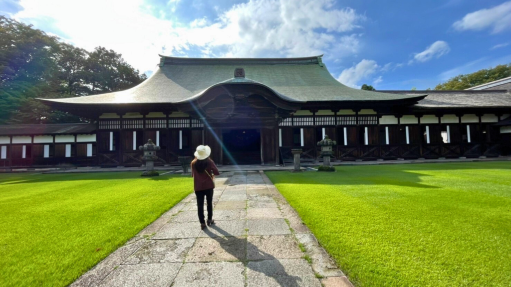 美しい芝生が広がる真ん中に一本道、その奥に大きなお寺があって、それに向かって歩く白い帽子の女性