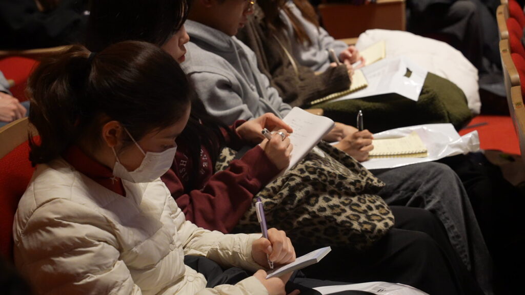 コンベンションのスピーチを聞いてメモをとる参加者たち