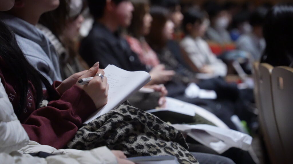 コンベンションのスピーチを聞きながらメモを取る来場者